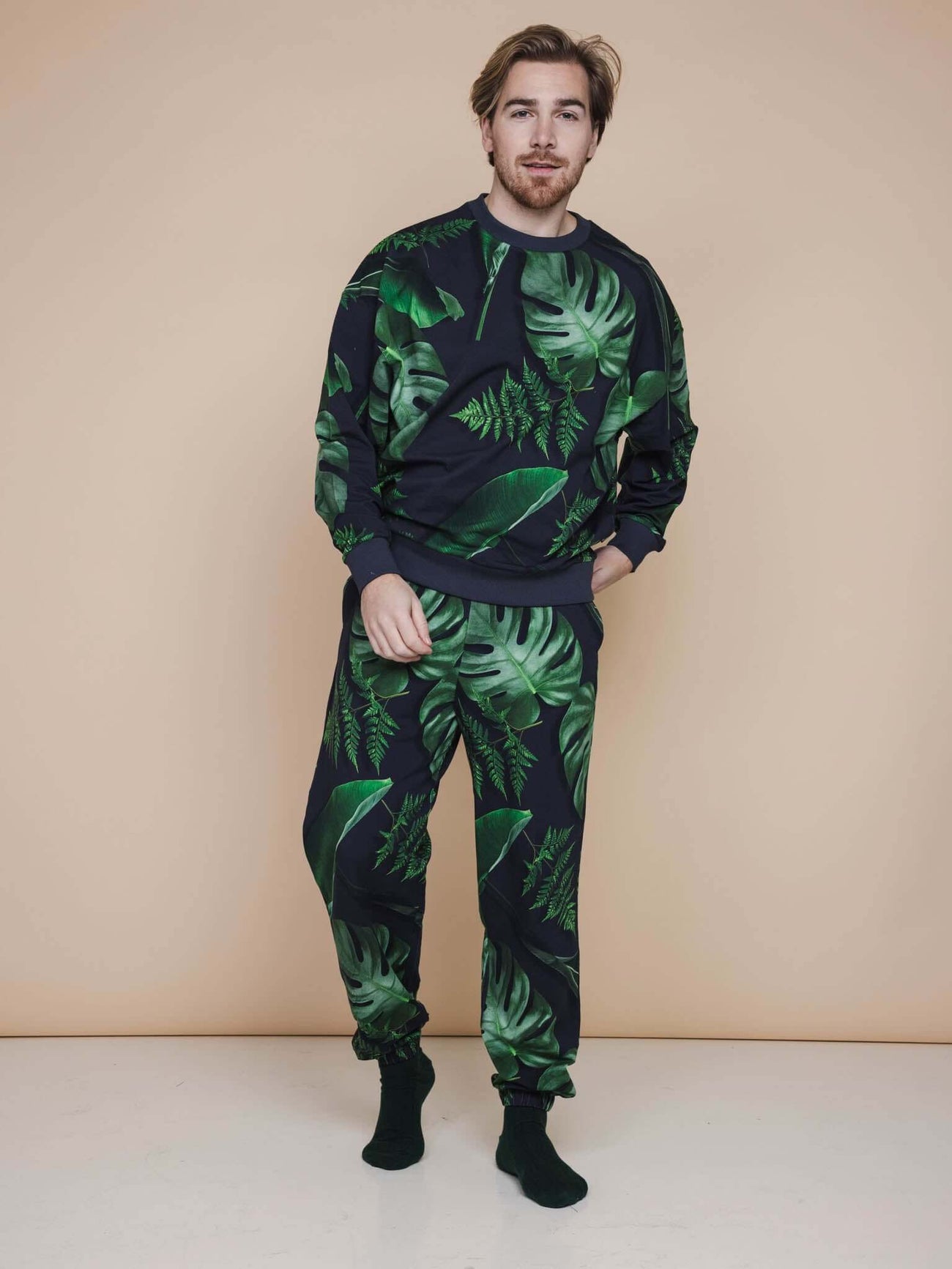 Model in SNURK Dark Forest Broek Relaxed Unisex met donkergroene bladerenprint op antracietgrijze achtergrond.