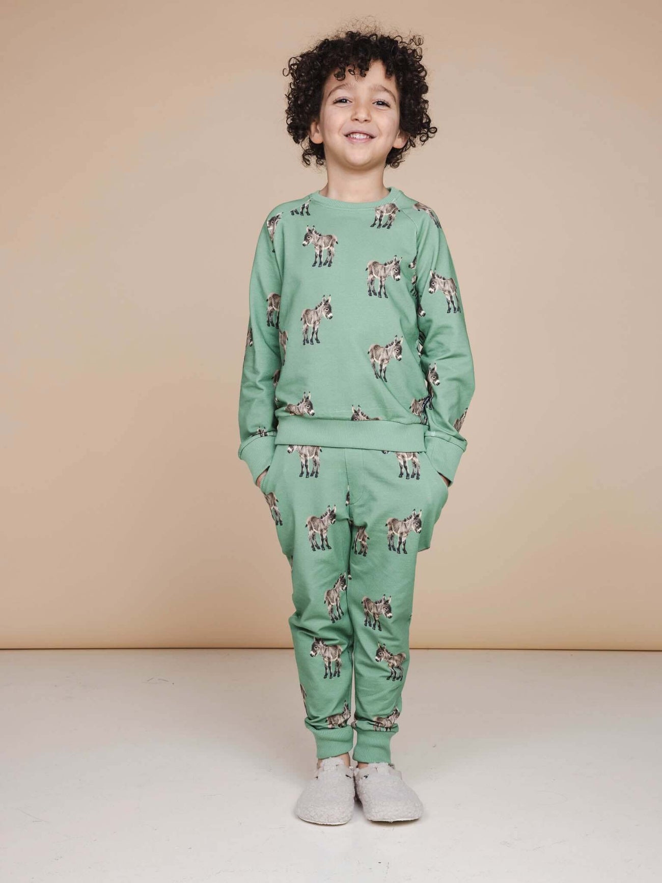 Kind in SNURK Donkeys Broek Kids, comfortabel in zachtgroene joggingoutfit met schattige ezels.