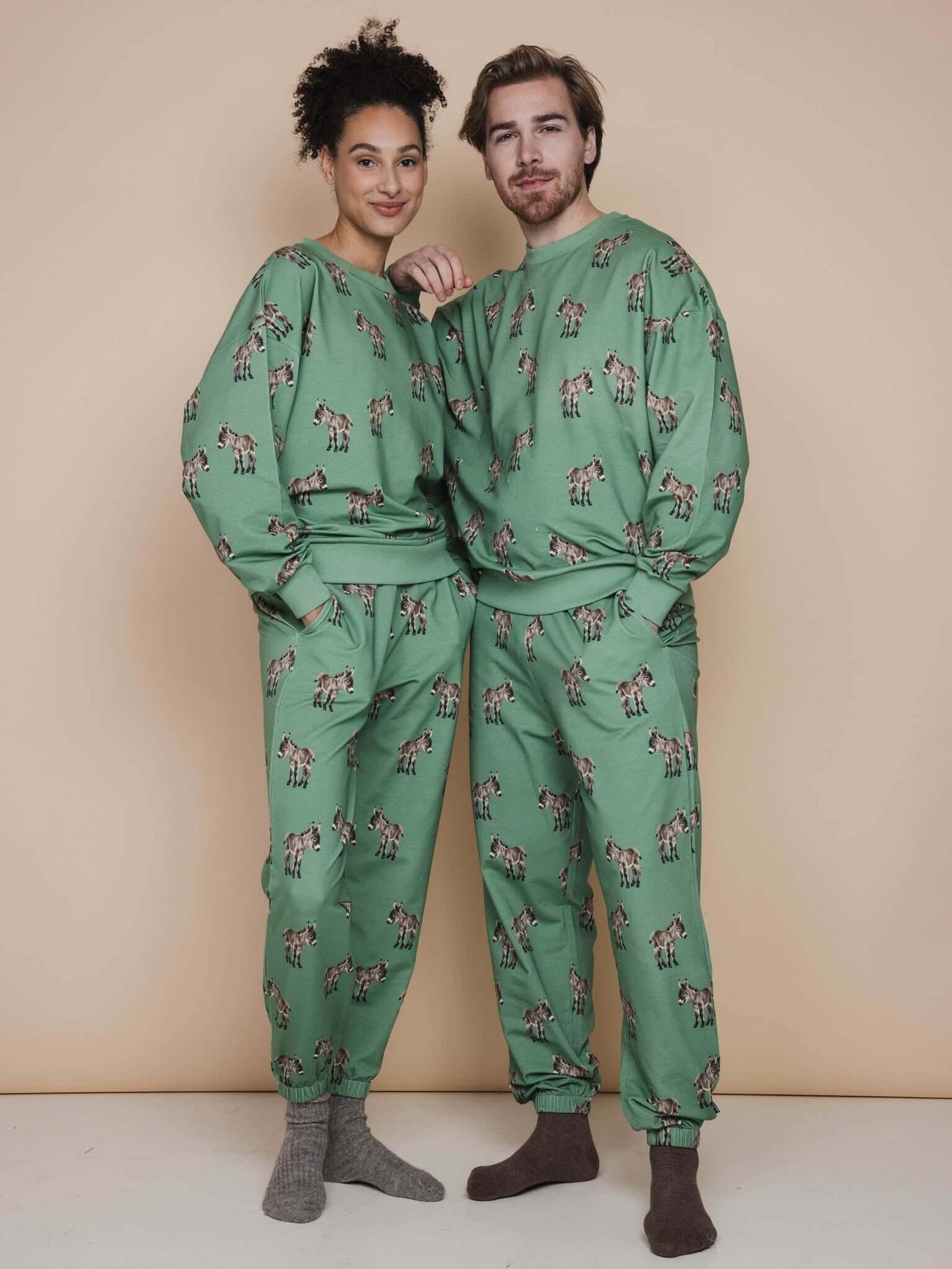 SNURK Donkeys Broek Relaxed Unisex in zachtgroene kleur met schattige baby-ezels, gedragen door een man en vrouw.