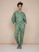 Vrouw in SNURK Donkeys Broek Relaxed Unisex met schattige baby-ezels op een zachtgroene achtergrond.