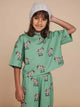 Kind in SNURK Donkeys Cropped T-Shirt Kids met schattige baby-ezels op een zachtgroene achtergrond.