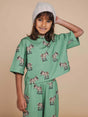 Kind in SNURK Donkeys Cropped T-Shirt Kids met schattige baby-ezels op een zachtgroene achtergrond.
