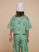 Een kind in een SNURK Donkeys Cropped T-Shirt Kids met schattige baby-ezels op een groen achtergron