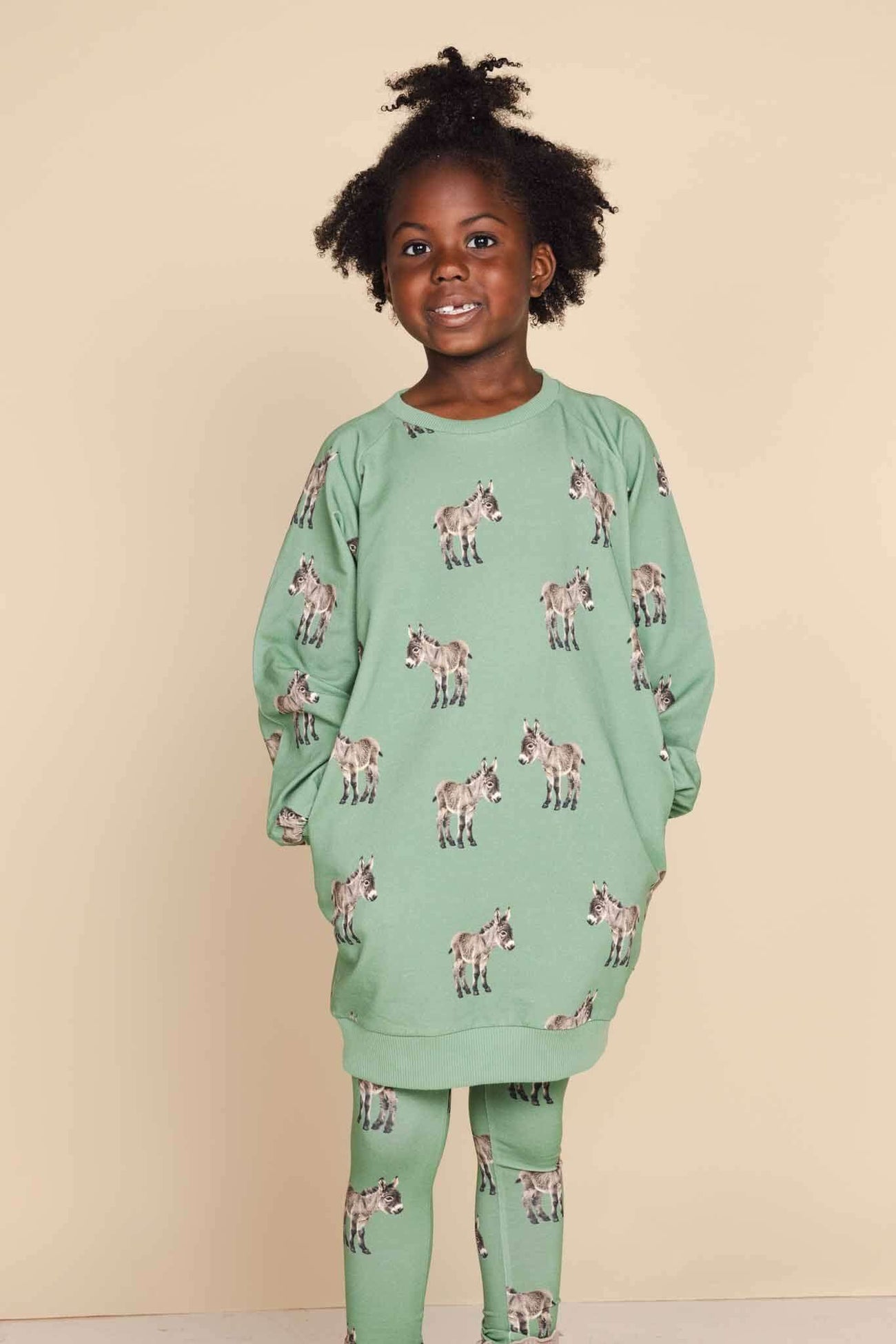 Kind in SNURK Donkeys Legging Kids met schattige baby-ezels op een zachtgroene achtergrond.