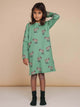 Kind in SNURK Donkeys Long Sleeve Dress Kids met schattige ezels op een zachtgroene achtergrond.