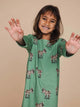 Een blije jongen in de SNURK Donkeys Long Sleeve Dress Kids met schattige ezels op een groene achtergrond.