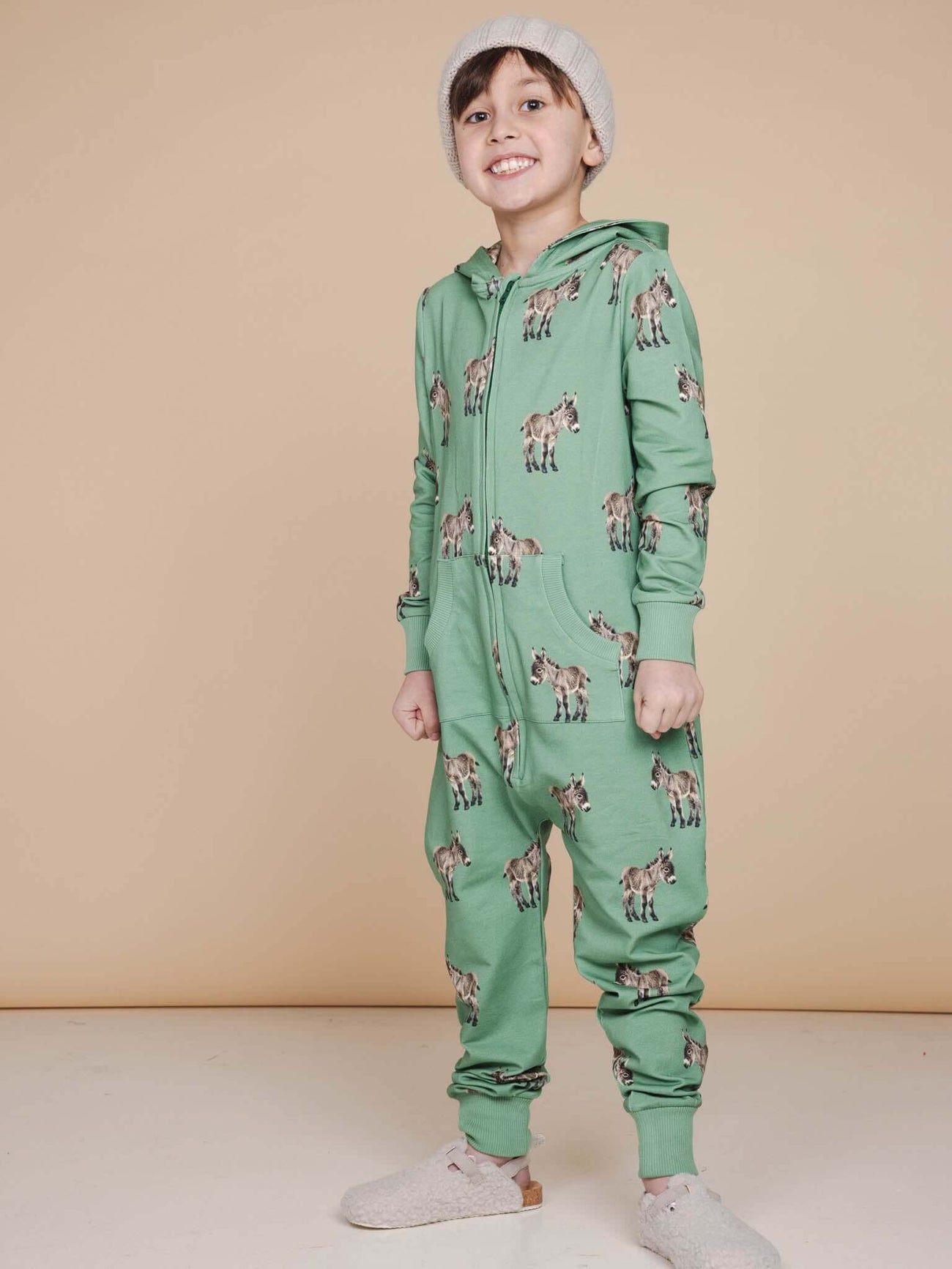 Kind in SNURK Donkeys Onesie Kids met schattige ezels op een zachte groene achtergrond.