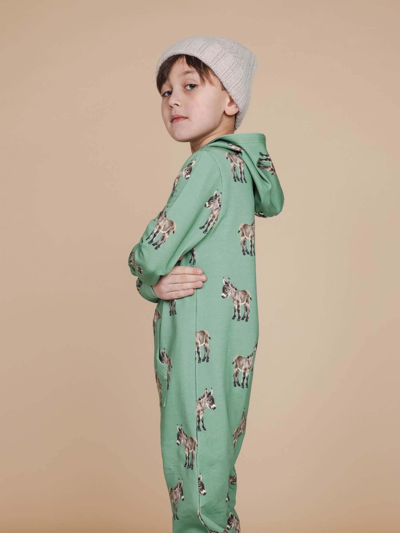 Jongen in SNURK Donkeys Onesie Kids met schattige baby-ezels op een zachtgroene achtergrond.
