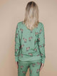 Een vrouw draagt de SNURK Donkeys Sweater Dames met schattige baby-ezels op een zachte groene achtergrond.