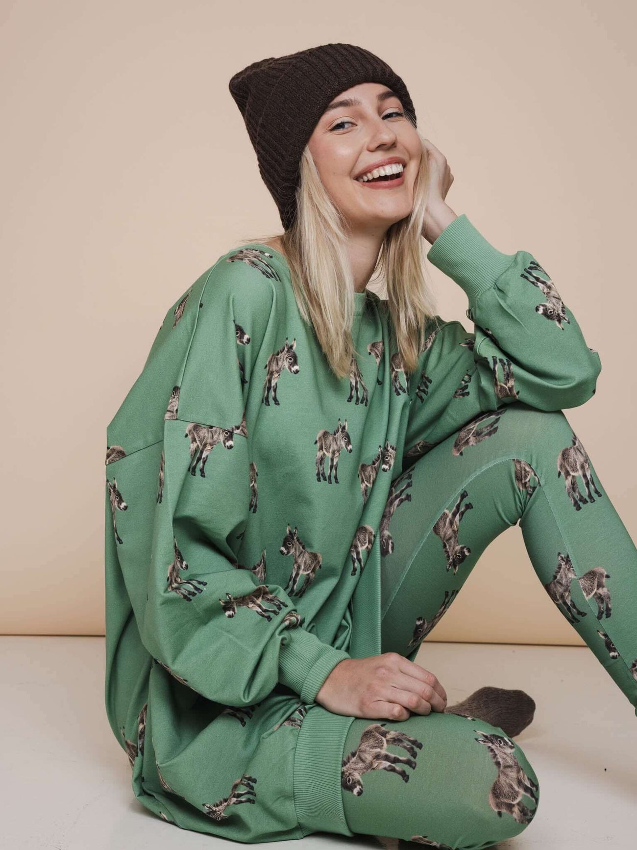 SNURK Donkeys Sweater Dress Dames gedragen door vrouw in groene outfit met ezelsprint en gebreide muts.