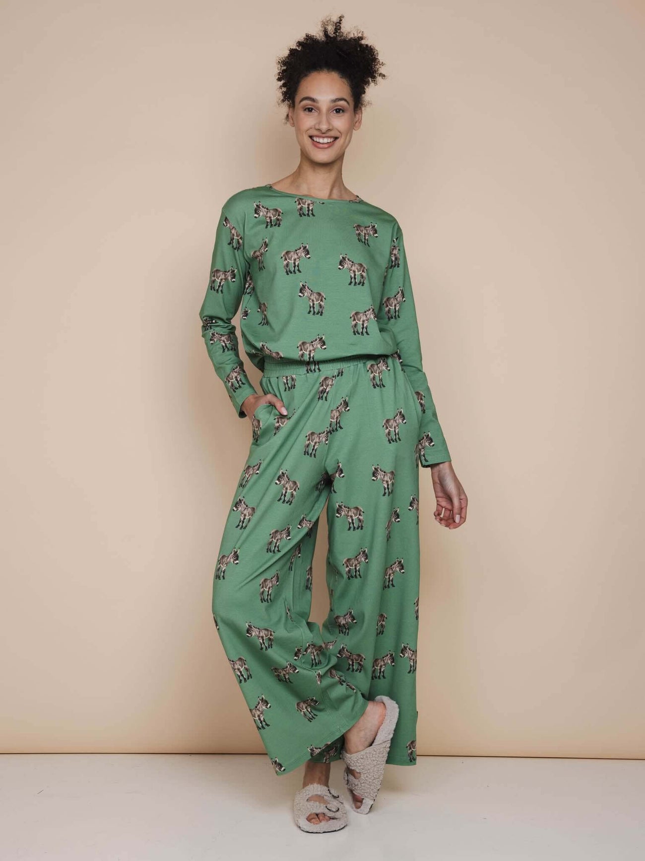 SNURK Donkeys Wijde broek Dames model in een schattige broek met baby-ezels op een zachtgroene achtergrond.