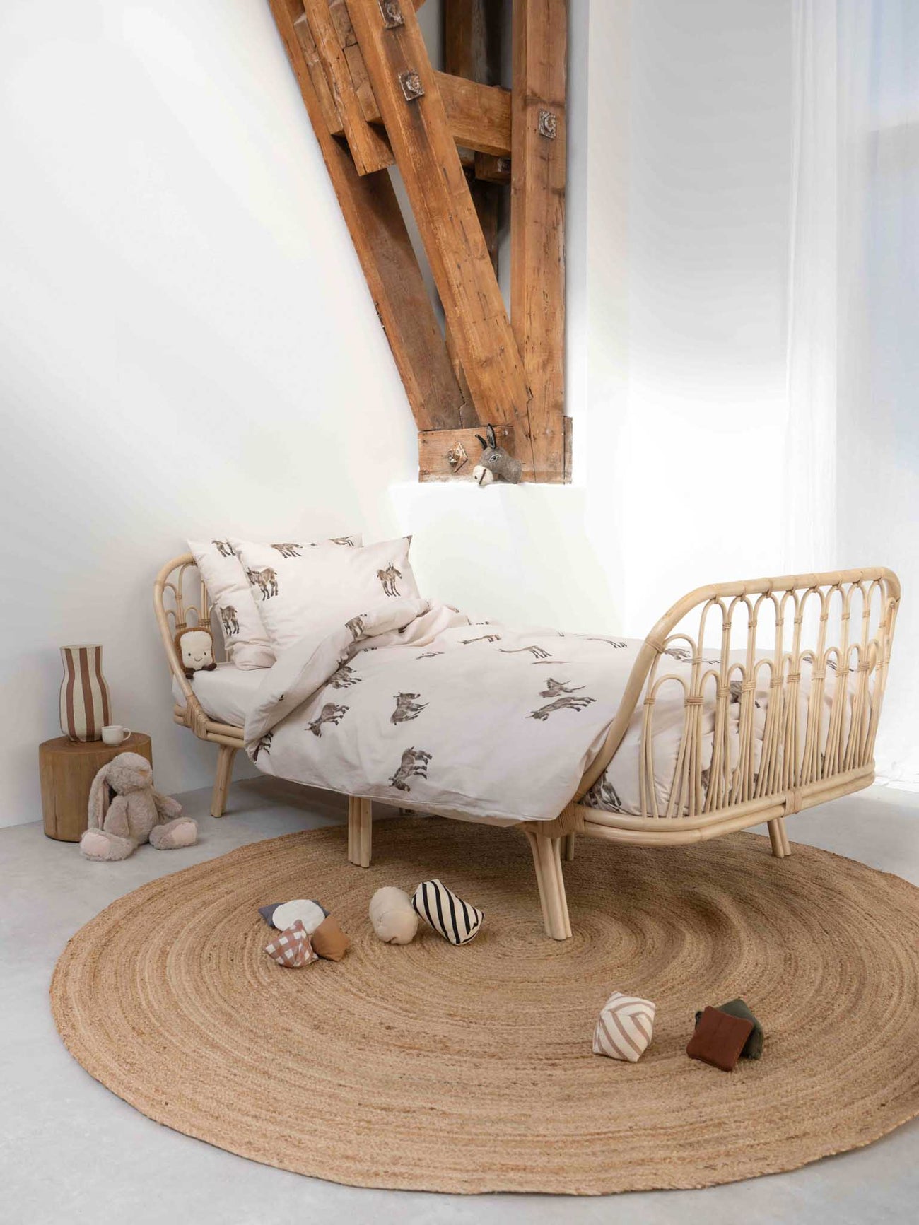 SNURK Donkeys dekbedovertrek op een bed met een rieten bedframe en speelse accessoires in een lichte slaapkamer.