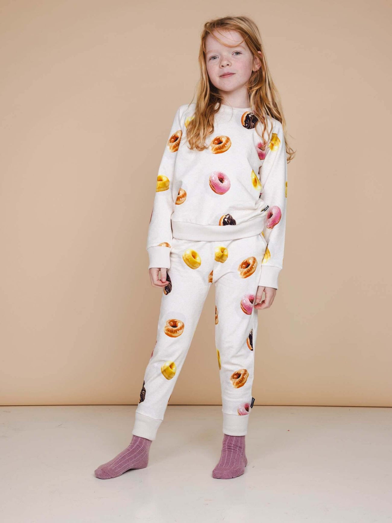 Kind met SNURK Donuts Broek Kids, vrolijke donuts print op een zachte beige achtergrond.