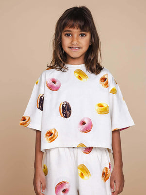 SNURK Donuts Cropped T-Shirt Kids worn by a smiling girl, featuring colorful donut print on a soft white fabric.