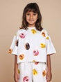 SNURK Donuts Cropped T-Shirt Kids worn by a smiling girl, featuring colorful donut print on a soft white fabric.