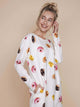 Vrolijke vrouw in SNURK Donuts Long Sleeve Dress Dames met kleurrijke donutprint op een zachte achtergrond.