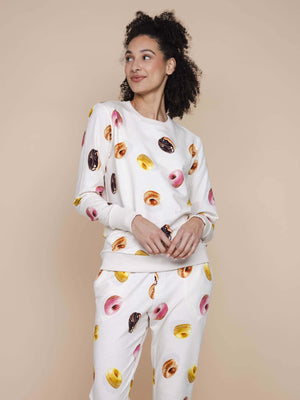 Model draagt de SNURK Donuts Sweater Dames met kleurrijke donut print op een beige achtergrond.