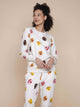 Model draagt de SNURK Donuts Sweater Dames met kleurrijke donut print op een beige achtergrond.