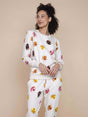 Model draagt de SNURK Donuts Sweater Dames met kleurrijke donut print op een beige achtergrond.