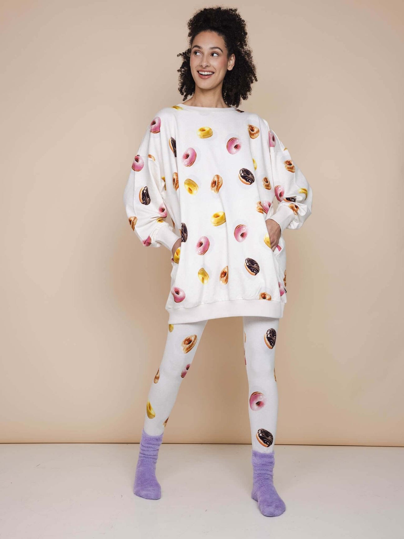 SNURK Donuts Sweater Dress Dames met donutprint op beige achtergrond, gedragen met bijpassende leggings.
