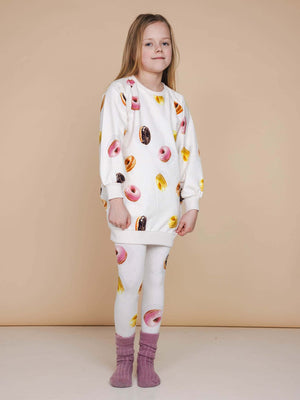 Een meisje in een SNURK Donuts Sweater Dress Kids met leggings, perfect voor chillen en slapen.