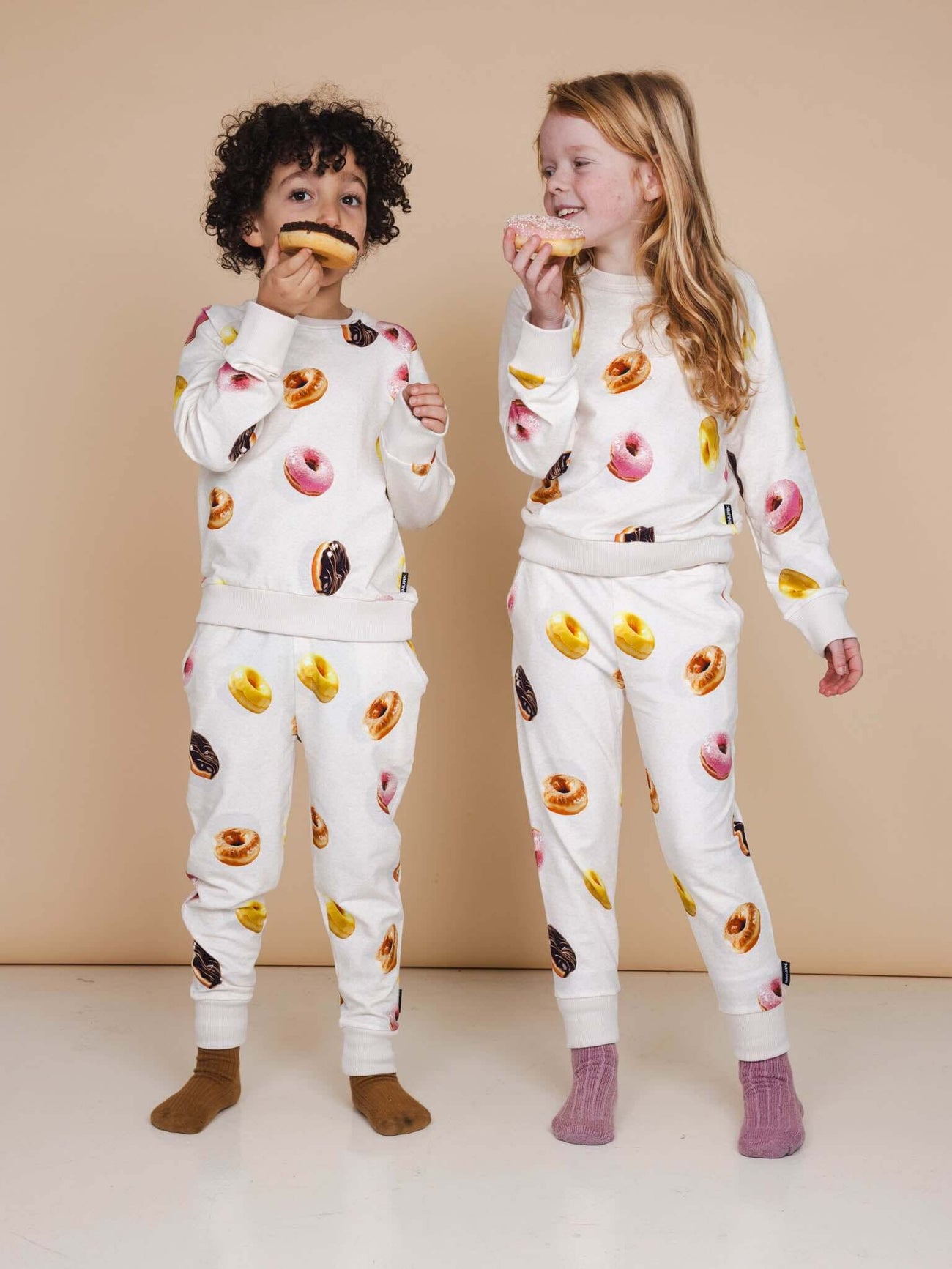 Kinderen in SNURK Donuts Sweater Kids met kleurrijke donuts op witte achtergrond.