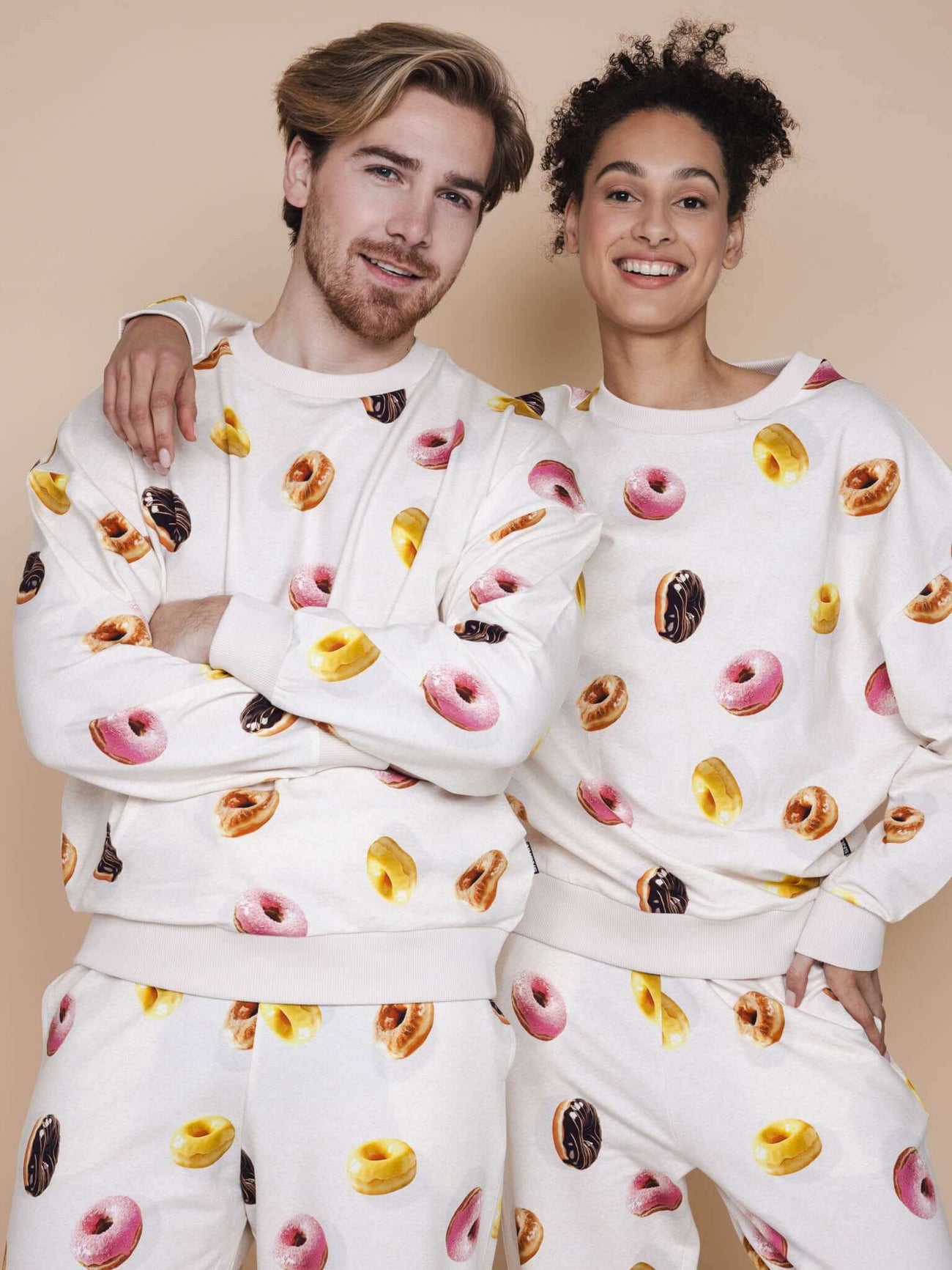 SNURK Donuts Sweater Unisex met kleurrijke donutprint, gedragen door model in beige achtergrond.