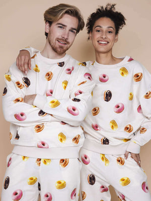 SNURK Donuts Sweater Unisex met kleurrijke donutprint, gedragen door model in beige achtergrond.