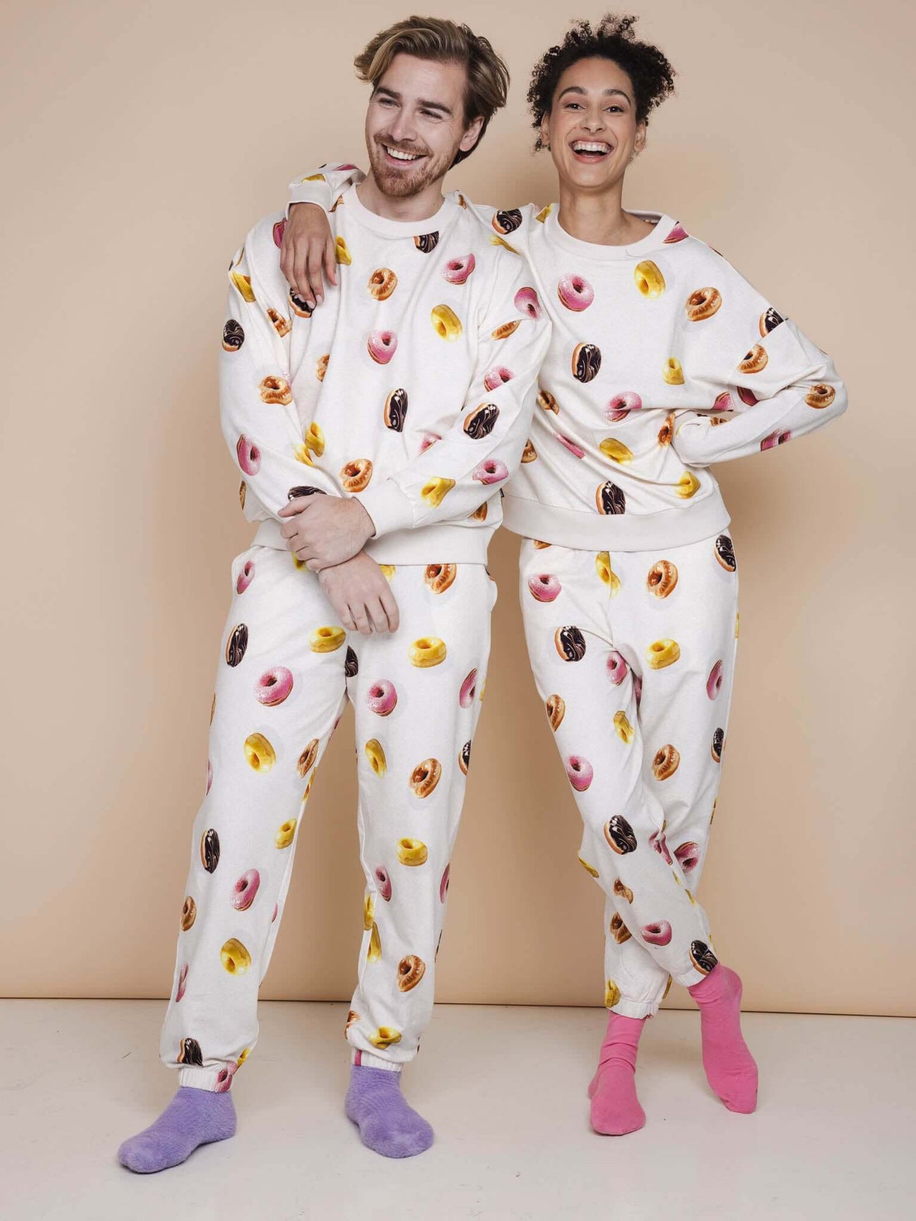 SNURK Donuts Sweater Unisex modelled by couple in colorful donut print on beige background.
