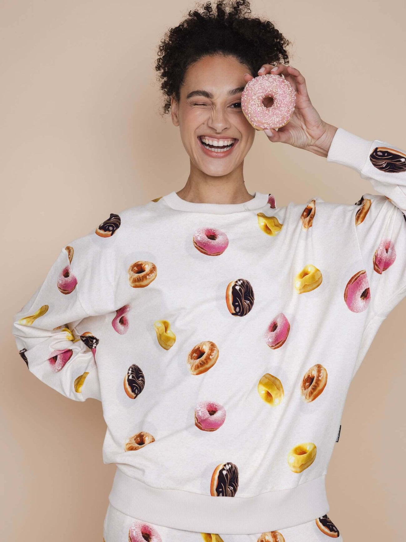 SNURK Donuts Sweater Unisex met kleurrijke donutprint, gedragen door een lachende vrouw.