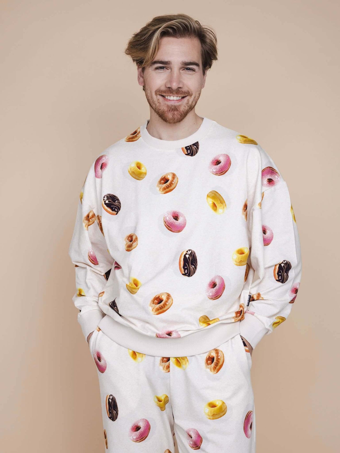 SNURK Donuts Sweater Unisex met kleurrijke donutprint op een zachte beige achtergrond.