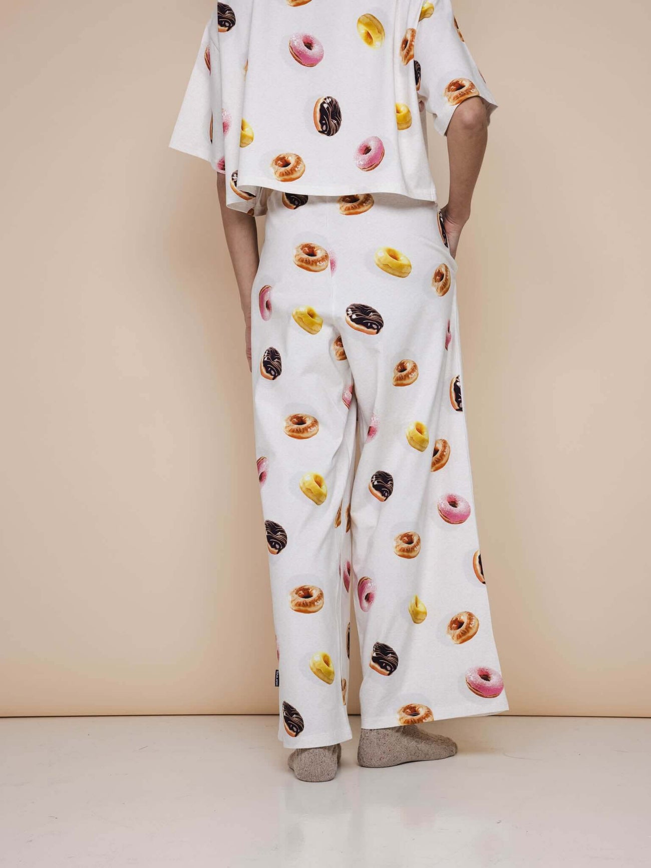 Afbeelding van de SNURK Donuts Wijde broek Dames met kleurrijke donutprint op een beige achtergrond.