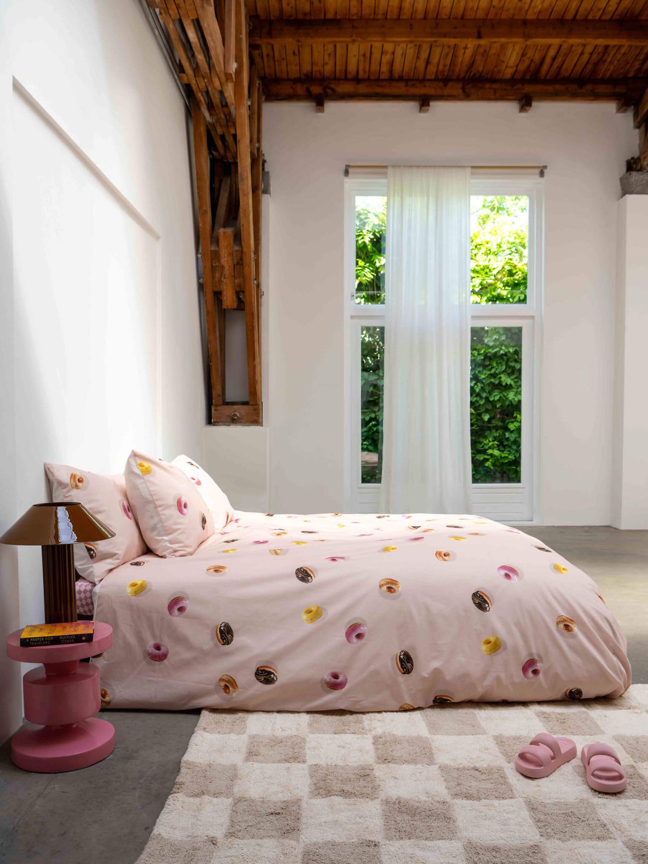SNURK Donuts dekbedovertrek op een bed met lichtroze ondergrond en kleurrijke donutspatroon.