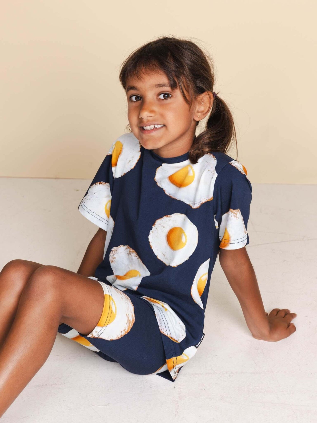 SNURK Eggs Navy T-shirt Kids gedragen door een vrolijk kind, met een design van spiegeleitjes op een navy achtergrond.