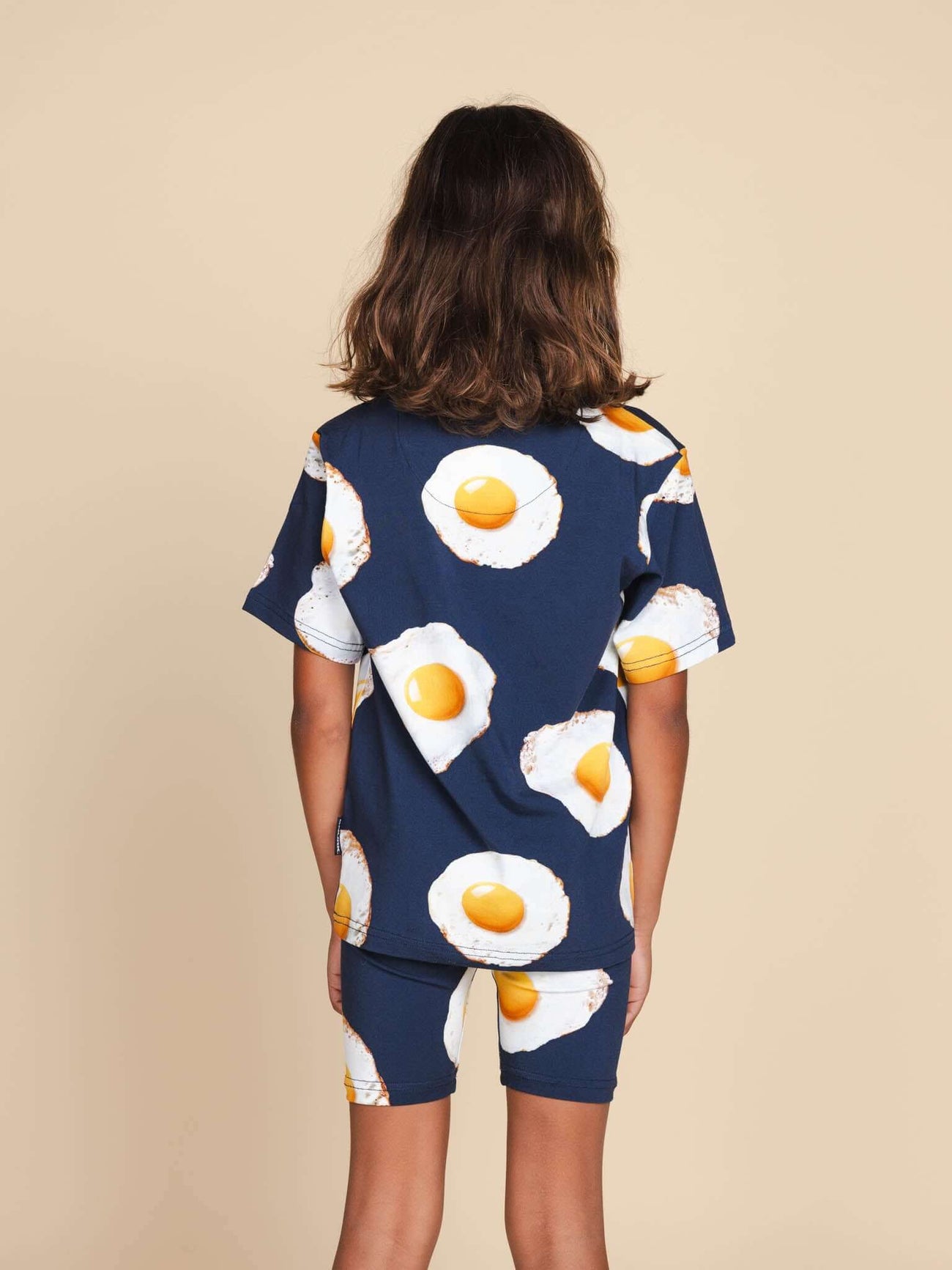 Kind in SNURK Eggs Navy T-shirt Kids met spiegeleitjesprint, achterkant zichtbaar met short.