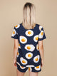 Achterkant van een vrouw die het SNURK Eggs Navy T-shirt Unisex draagt met spiegeleitjes op een blauwe achtergrond.