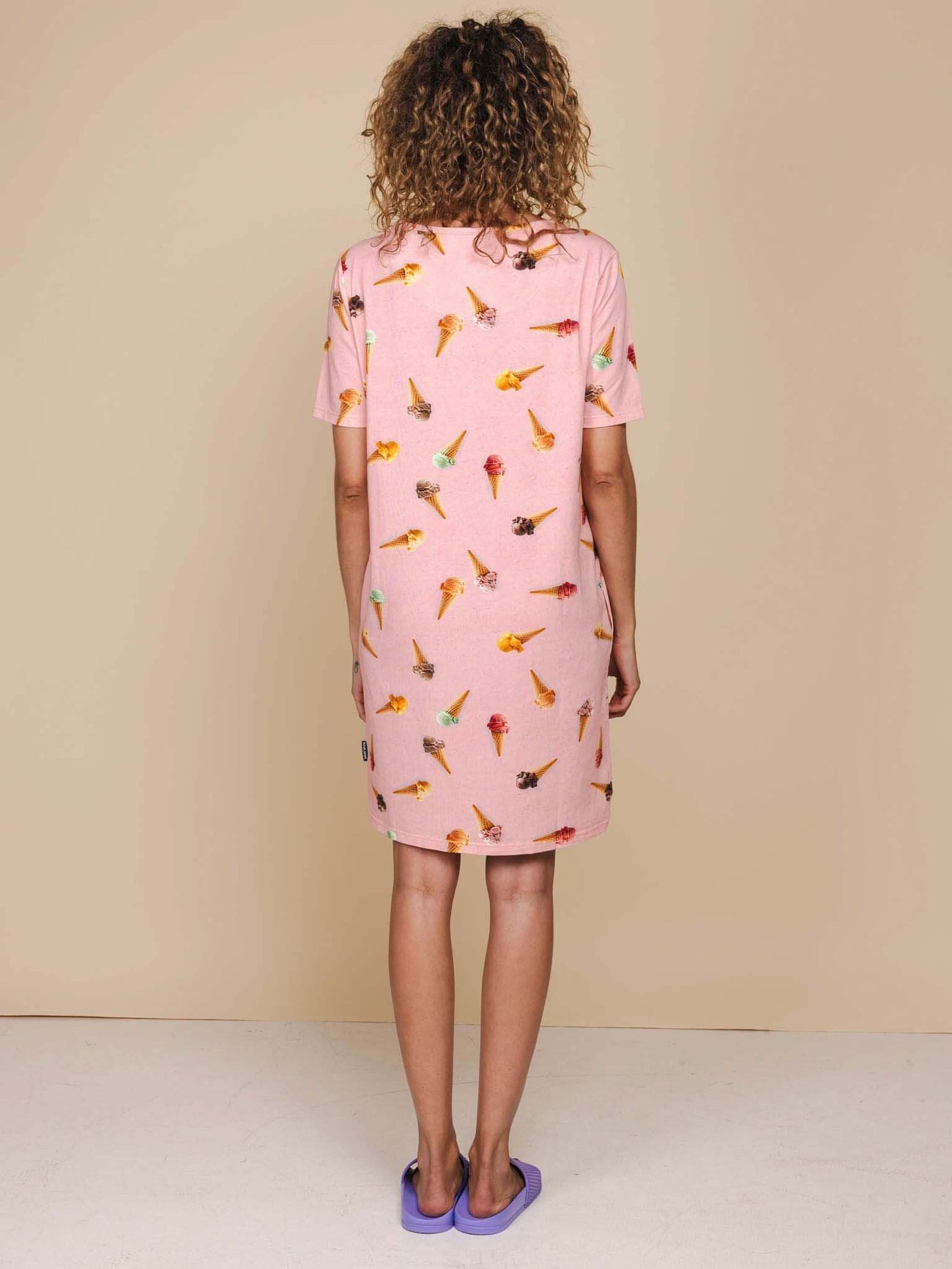 Model met krullend haar draagt de SNURK Ice Cream Cones T-shirt Dress Dames, roze met ijsjesprint.