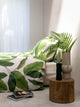 SNURK Leaf Me dekbedovertrek met bladerenprint op bed en decoratieve planten.
