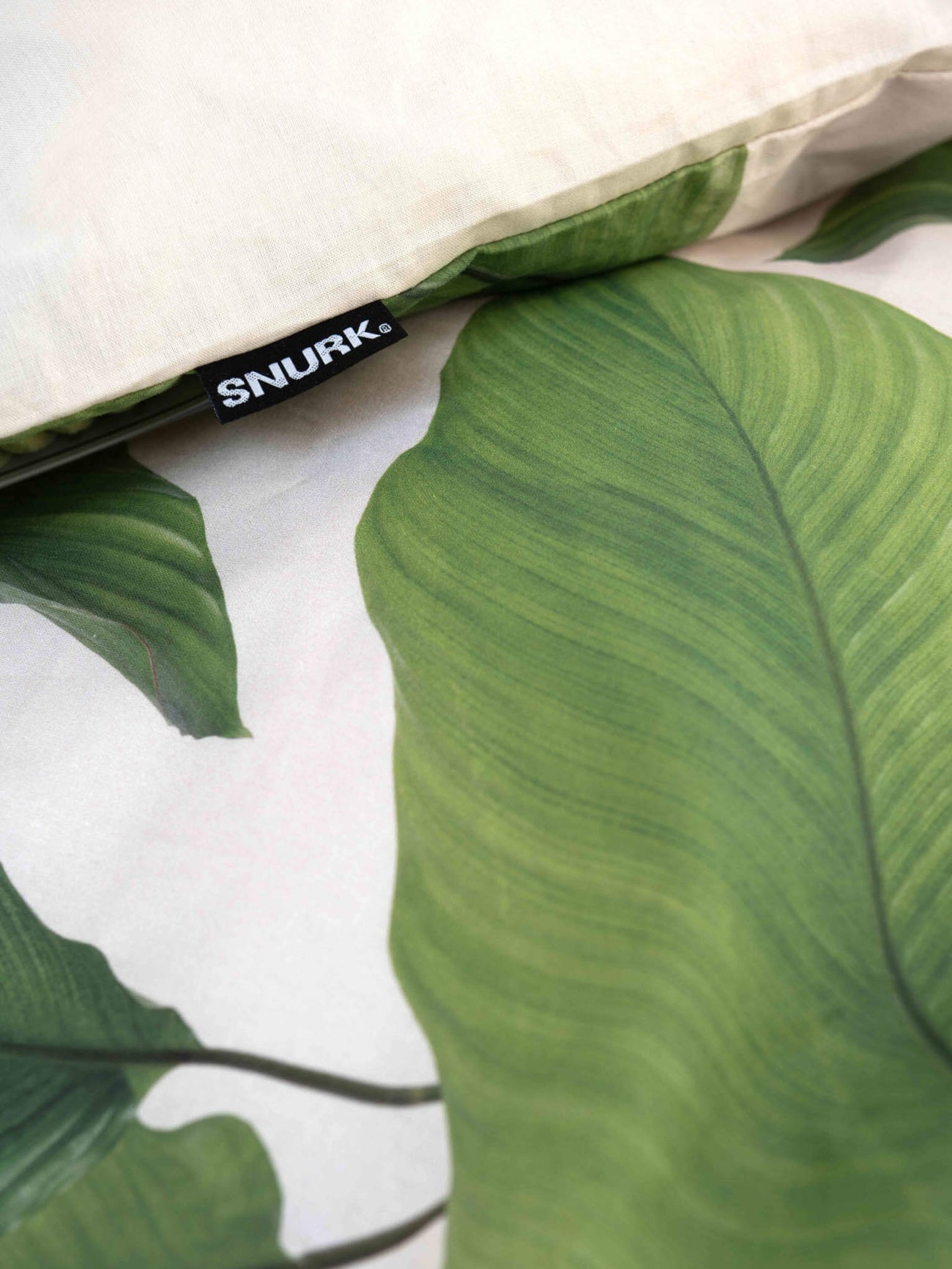 Detail van SNURK Leaf Me dekbedovertrek met dagelijkse bladerenprint en het merklabel.