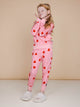 SNURK Lollipop Love Broek Kids - Meisje in felrode hartjeslollies broek op roze achtergrond.