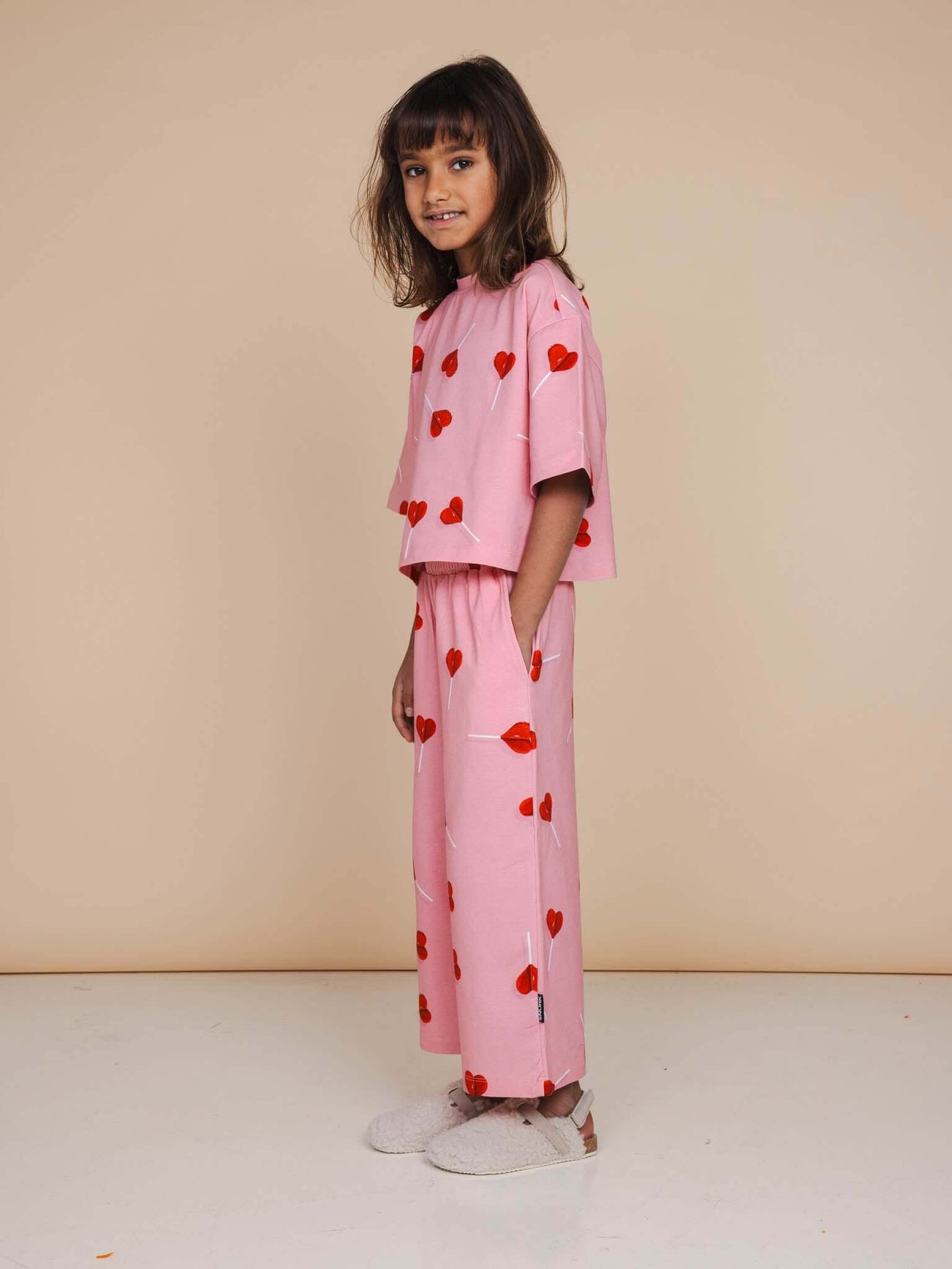 SNURK Lollipop Love Cropped T-Shirt Kids met rode hartjeslollies op roze, perfect voor vrolijke kindermomenten.