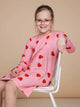 Meisje in SNURK Lollipop Love Long Sleeve Dress Kids met hartjeslollies op roze, zittend op een witte stoel.