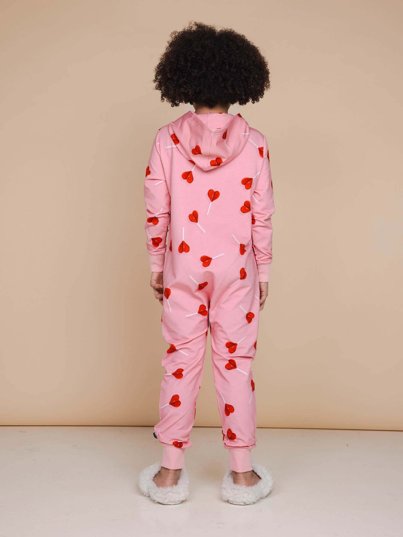 A child wearing a SNURK Lollipop Love Onesie Kids with red heart lollipops pattern, perfect for sleeping or playing.
