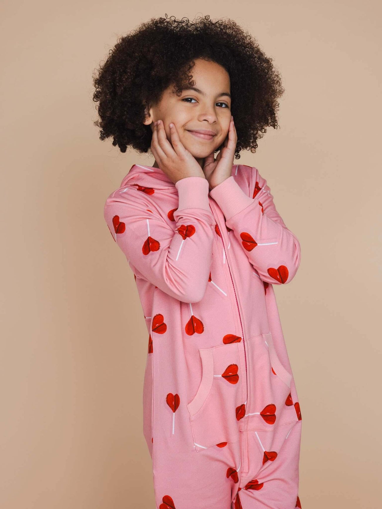 SNURK Lollipop Love Onesie Kids in roze met hartjeslollies op een kind met een vrolijke uitstraling.