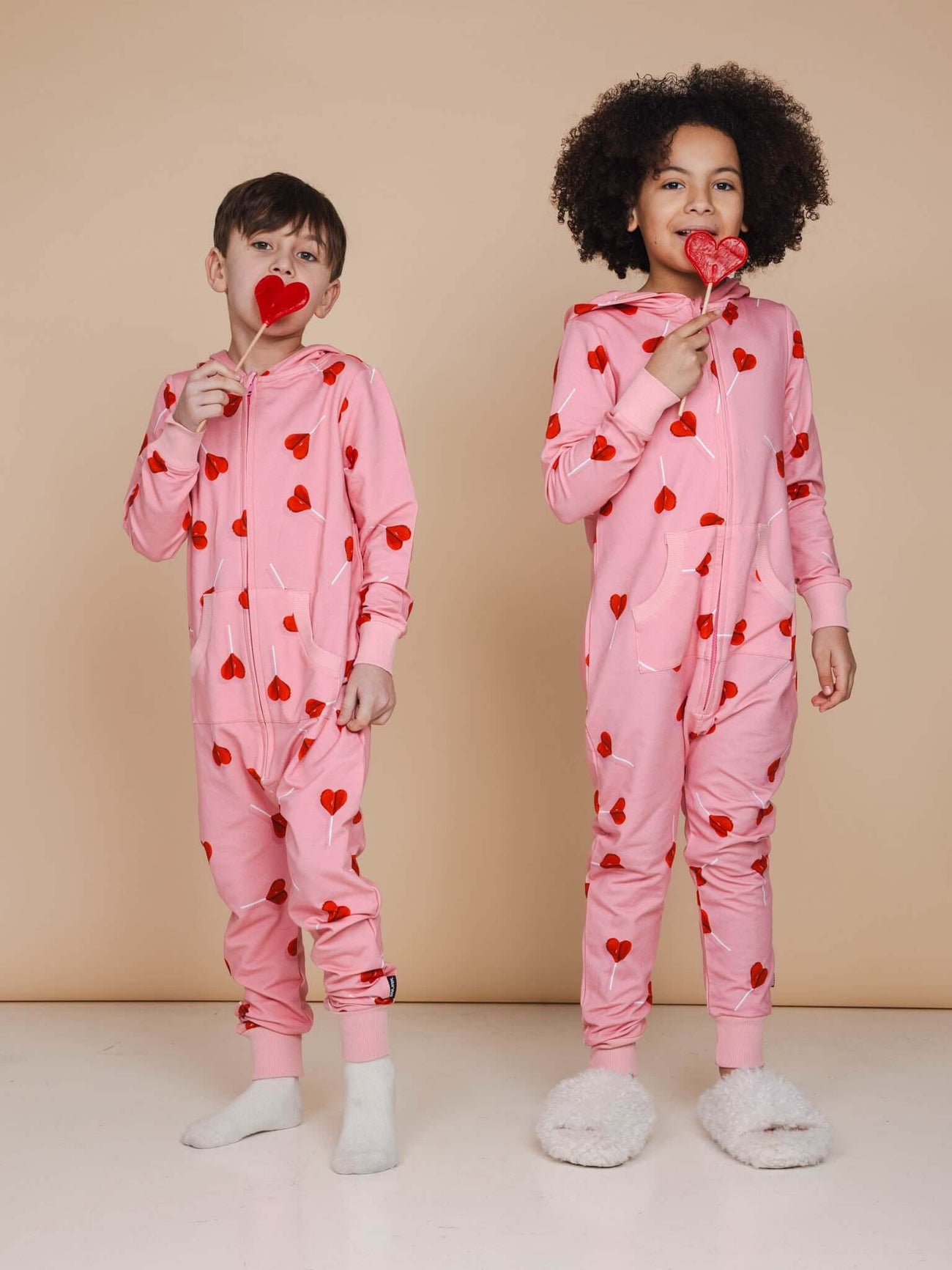 Kinderen in SNURK Lollipop Love Onesie Kids met hartjeslollies op een roze achtergrond.