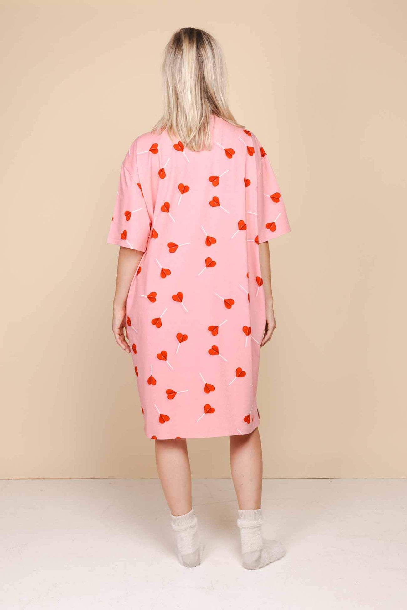 Model draagt SNURK Lollipop Love Relaxed Tee Dress Dames met felrode hartjeslollies op een roze achtergrond.
