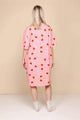 Model draagt SNURK Lollipop Love Relaxed Tee Dress Dames met felrode hartjeslollies op een roze achtergrond.