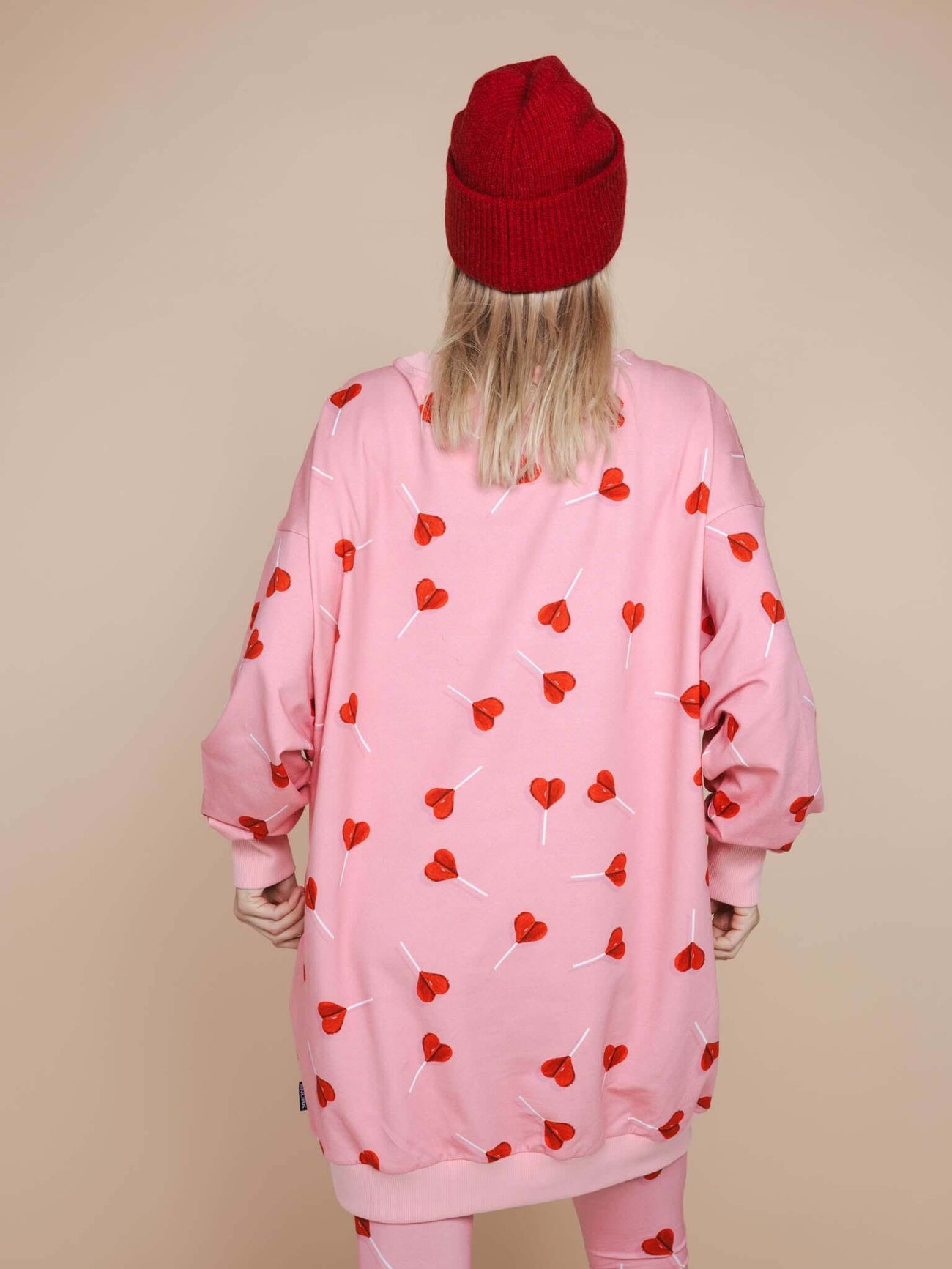 Achterkant van de SNURK Lollipop Love Sweater Dress Dames met hartjeslollies op een roze achtergrond, casual look.