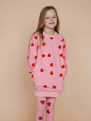  meisje in SNURK Lollipop Love Sweater Dress Kids met hartjeslollies op een roze achtergrond
