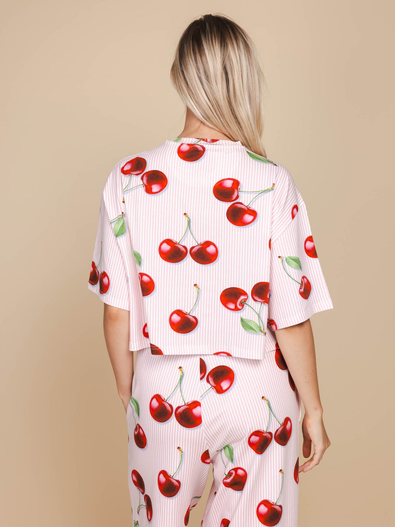 Vrouw met SNURK Mon Cherry Cropped T-Shirt Dames met kersenprint op een neutrale achtergrond.